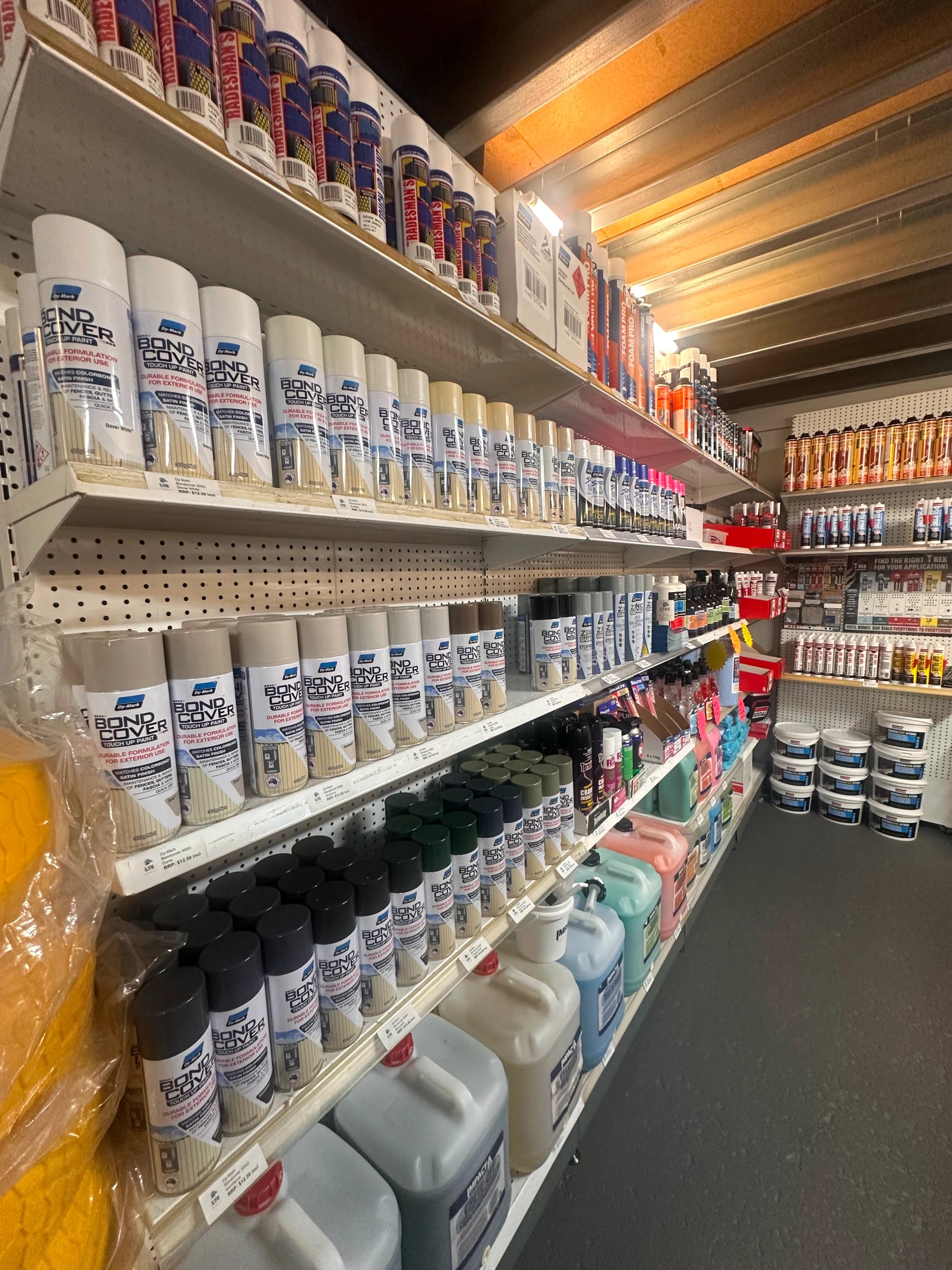 Store shelves stocked with various cans of spray paint, large plastic containers, and paint supplies.
