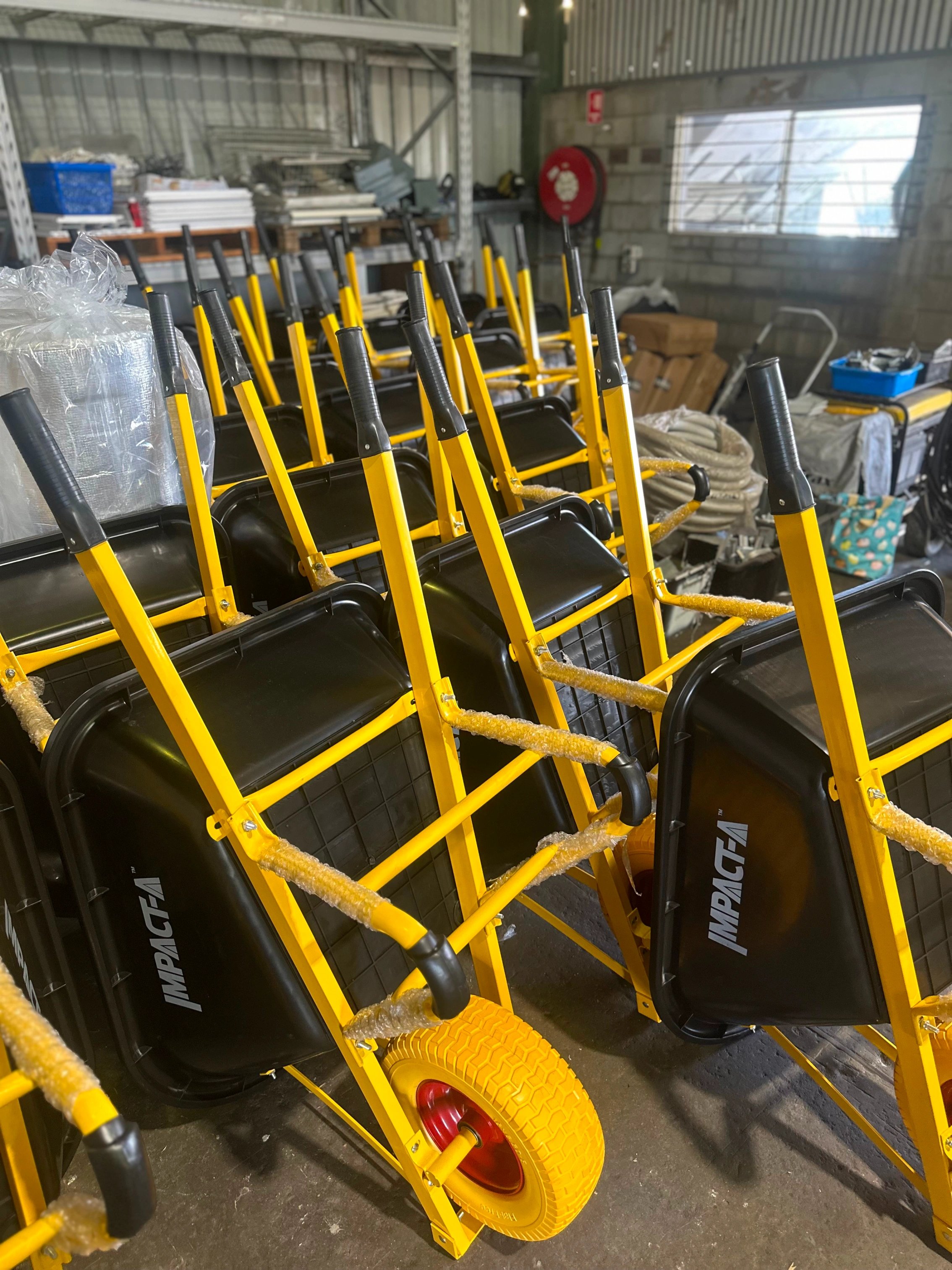 Several yellow wheelbarrows with black tubs and yellow wheels stacked inside a warehouse.