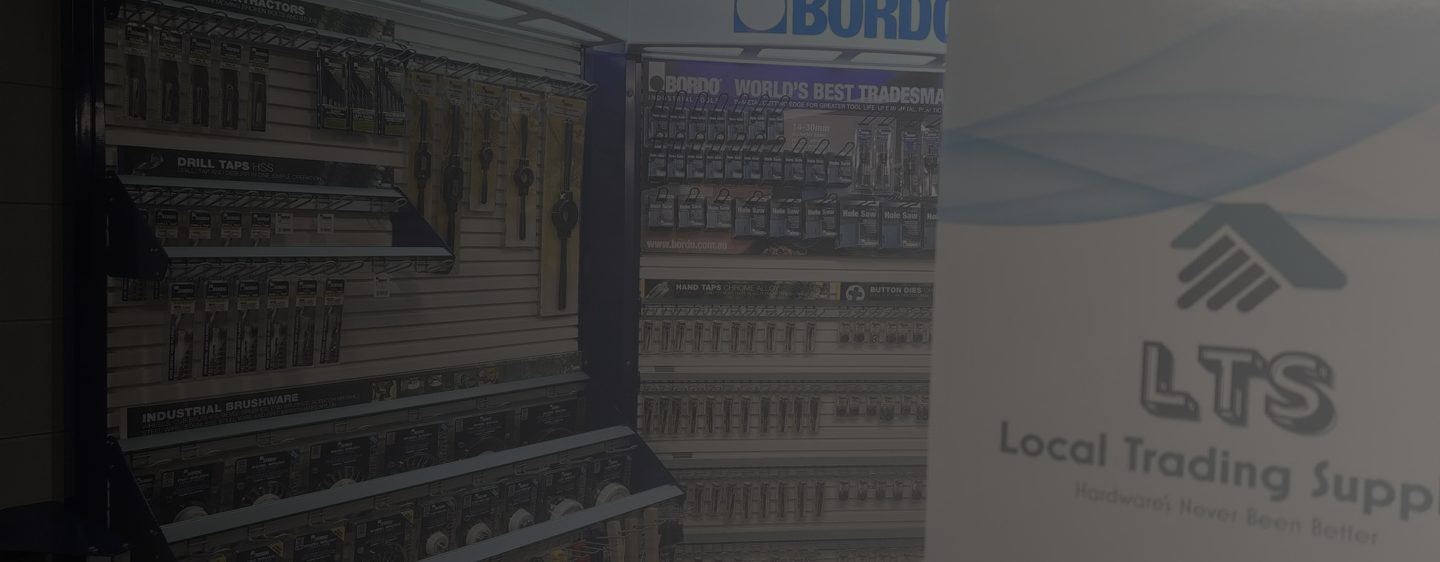 Display shelves with various drill taps, industrial brushware, hand taps, button dies, and hole saws in a hardware store.