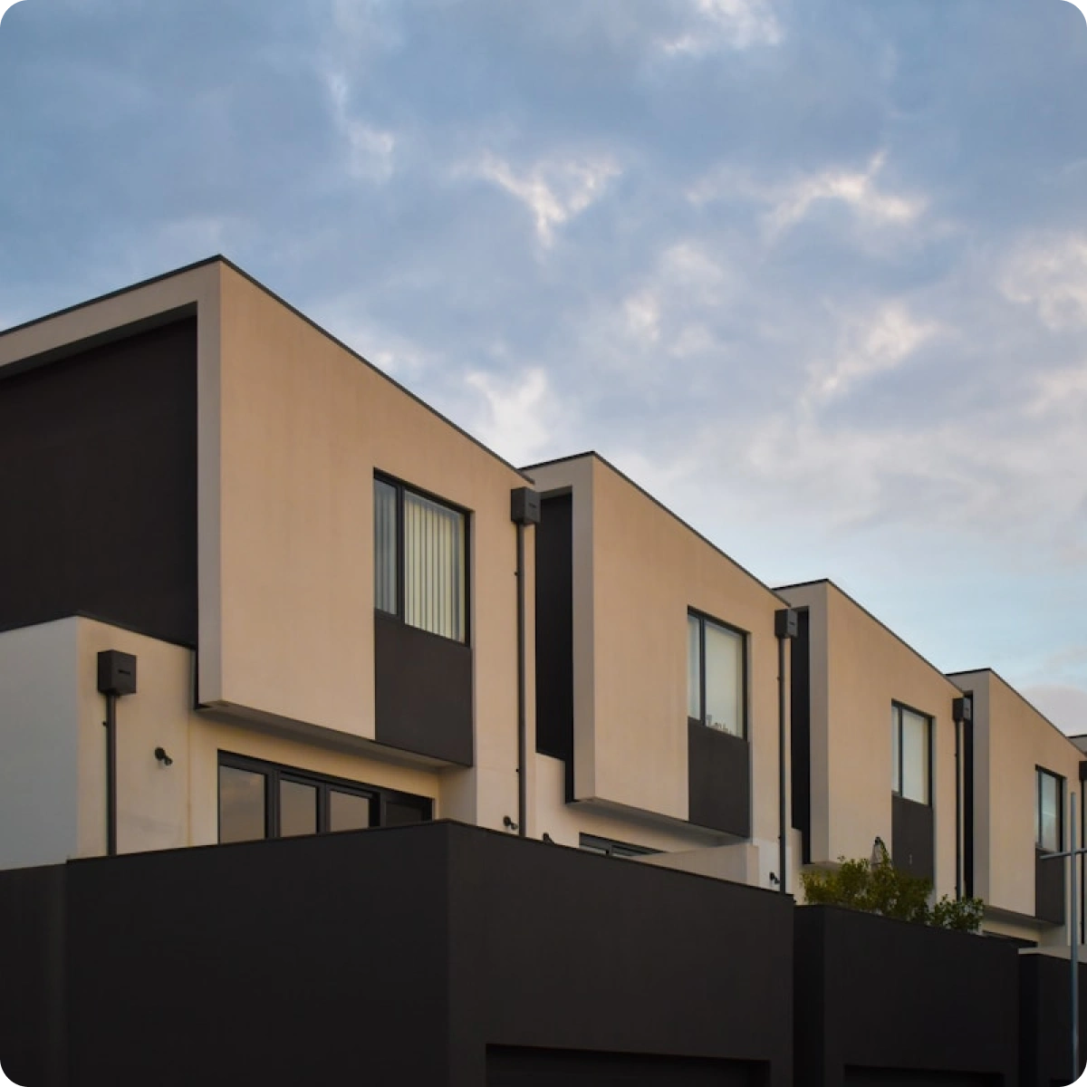 Modern two-story row of townhouses with beige and dark gray exteriors under a cloudy sky.