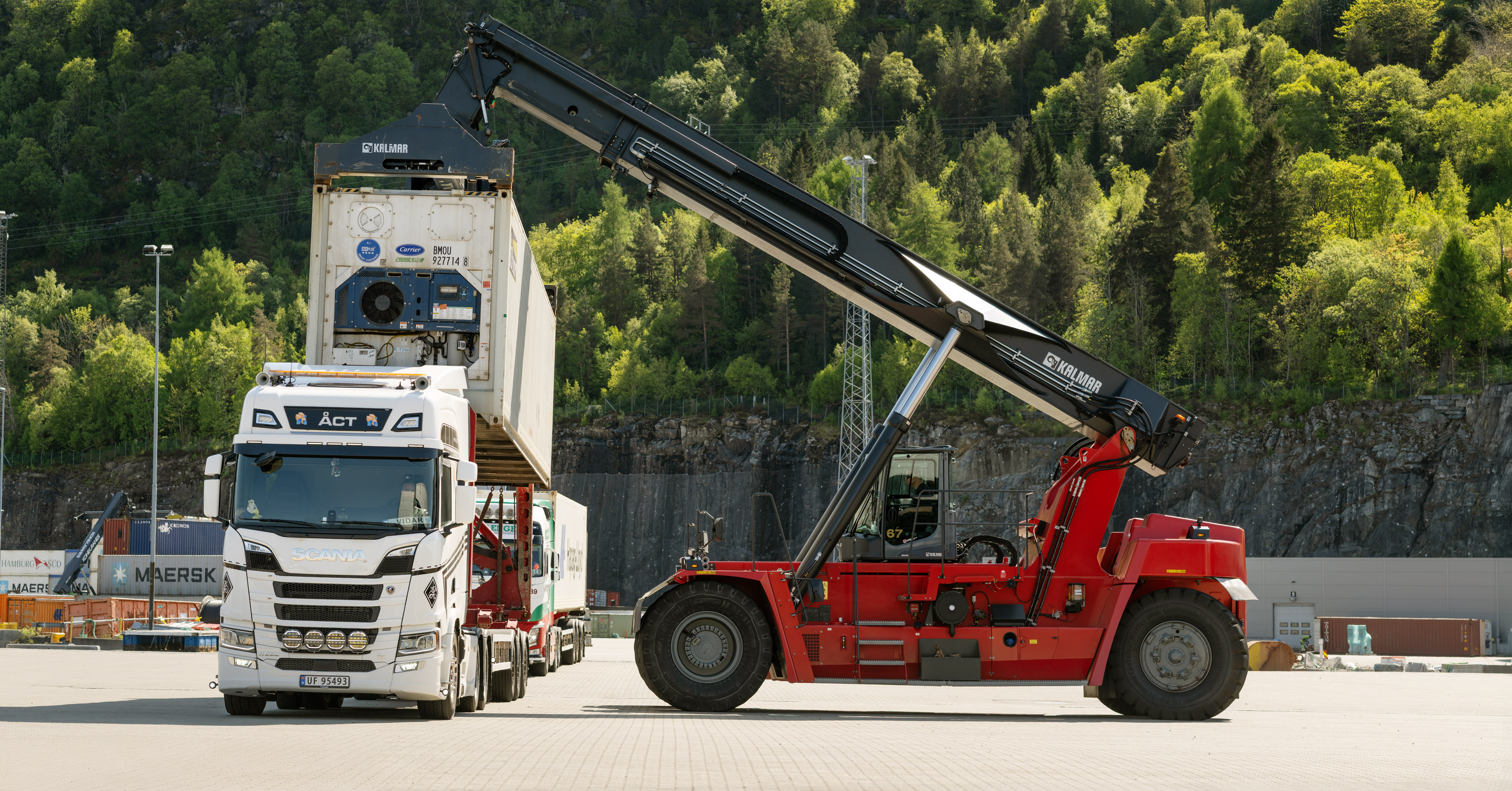 Reach stacker handling cargo beside a truck at the terminal