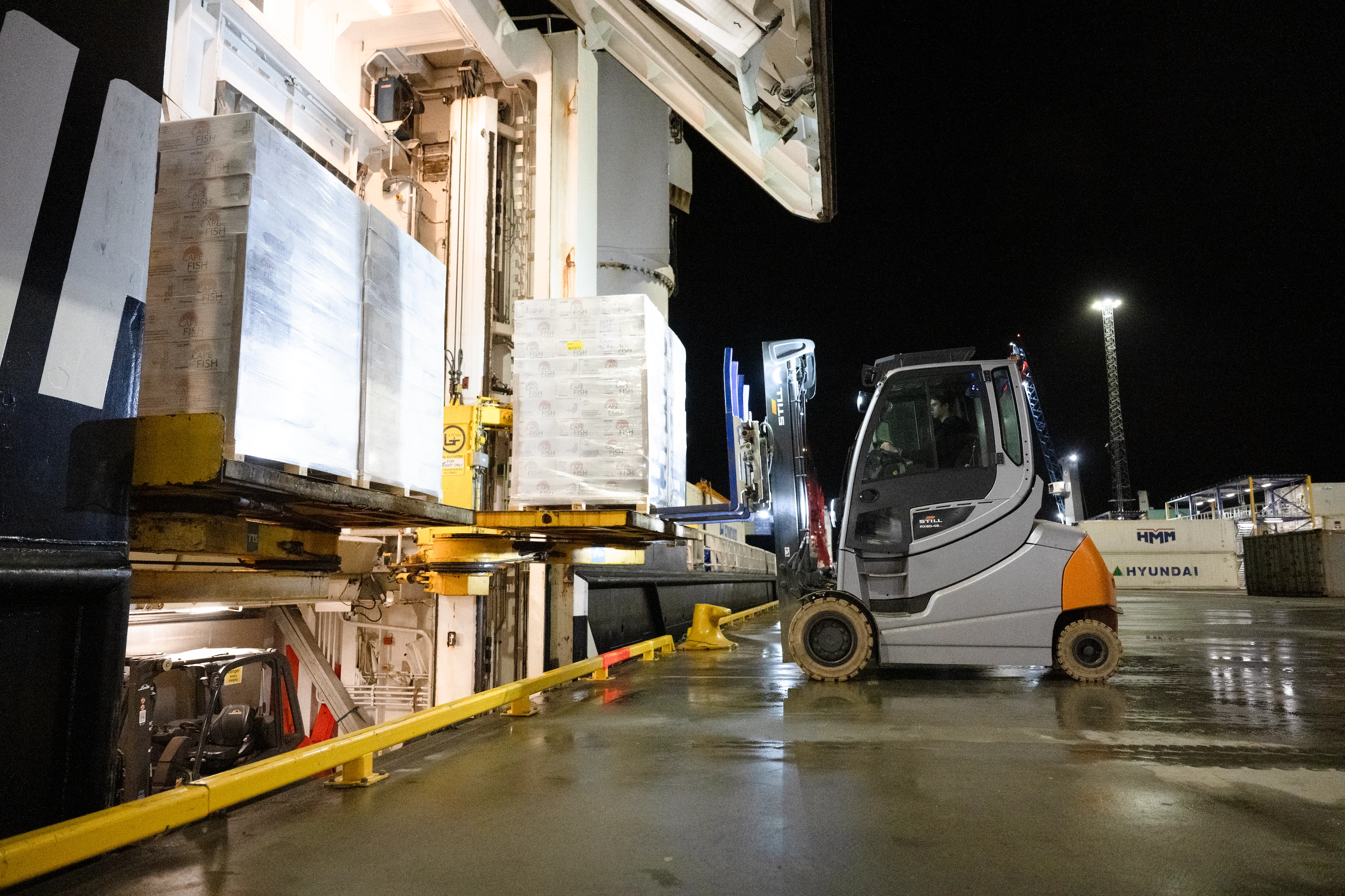 Gaffeltruck laster paller om bord i et skip om natten