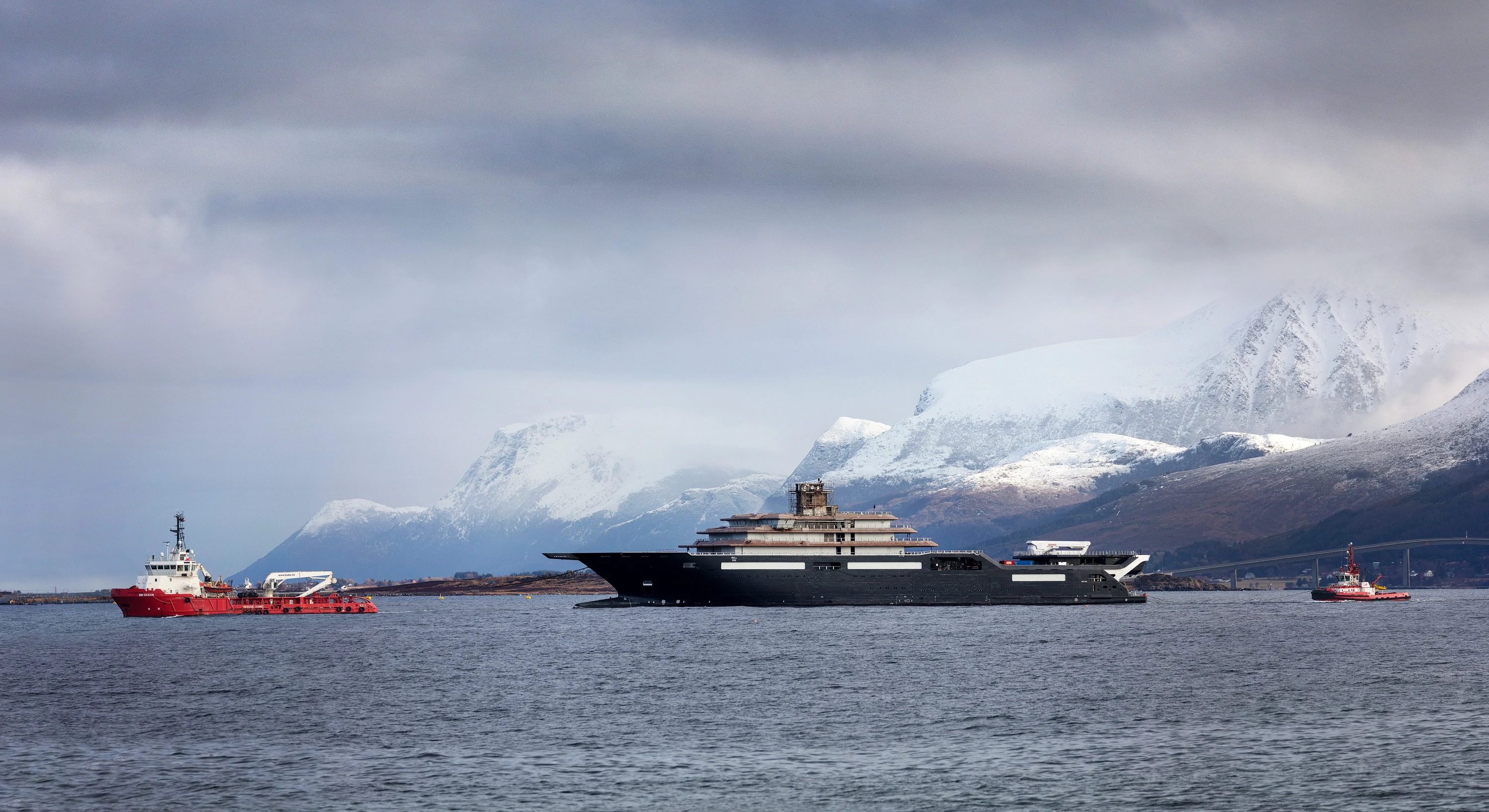 Ship and tugboats on the fjord with snow-covered mountains