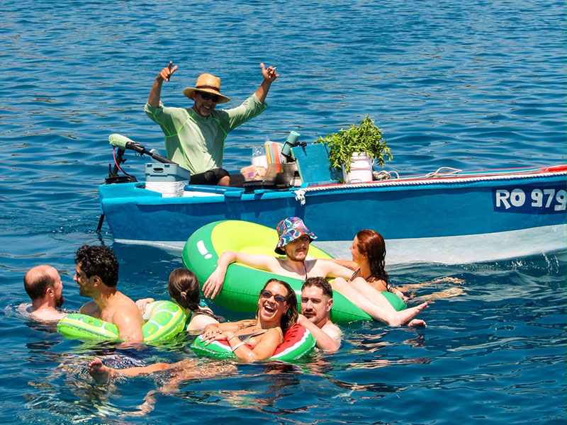 A group of ctrl alt sail attendees laughing togeter in the water, floating around the famous mojito man's boat awaiting their order