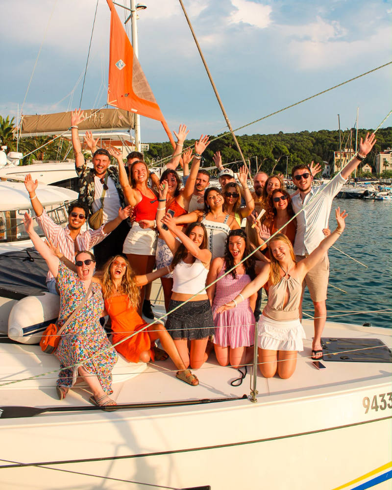 A group of ctrl.alt Sail attendees standing on one of the yachts in the sunshine, all with their hands raised