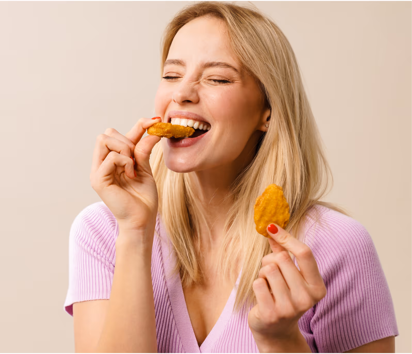 Smiling blonde woman in a pink sweater eating chicken nuggets with eyes closed.