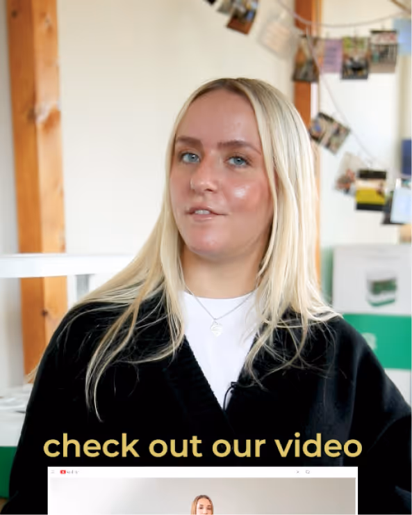Young blonde woman wearing a black jacket and white top sitting indoors with a string of photos pinned on the wall behind her, overlaid text reads 'check out our video'.