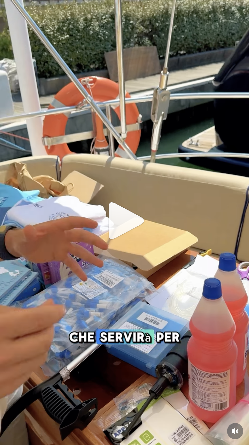 Mani su tavolo di barca con materiali da lavoro e bottiglie rosa vicino a salvagente arancione.