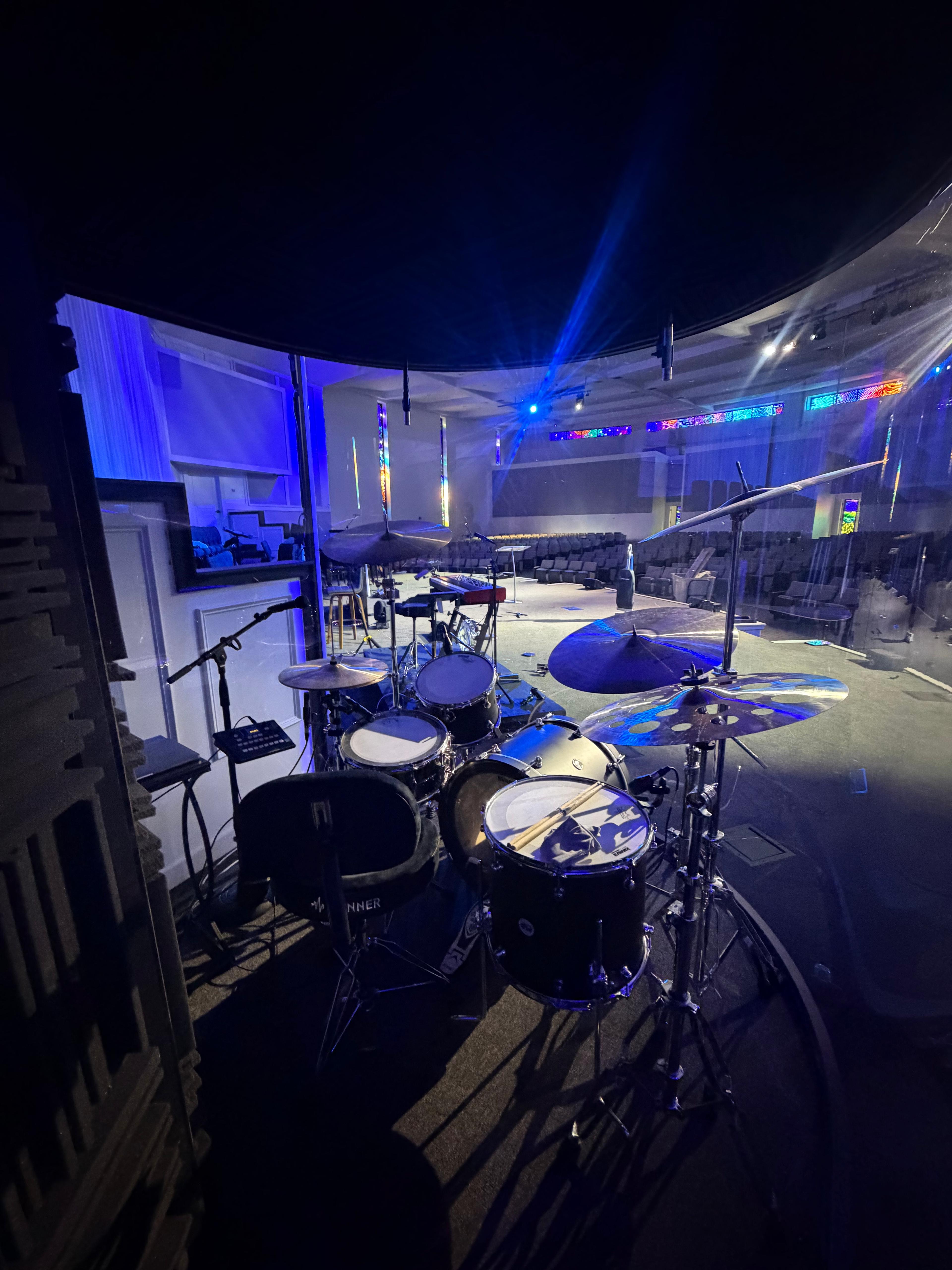 Drum kit inside an enclosure on a blue-lit church stage