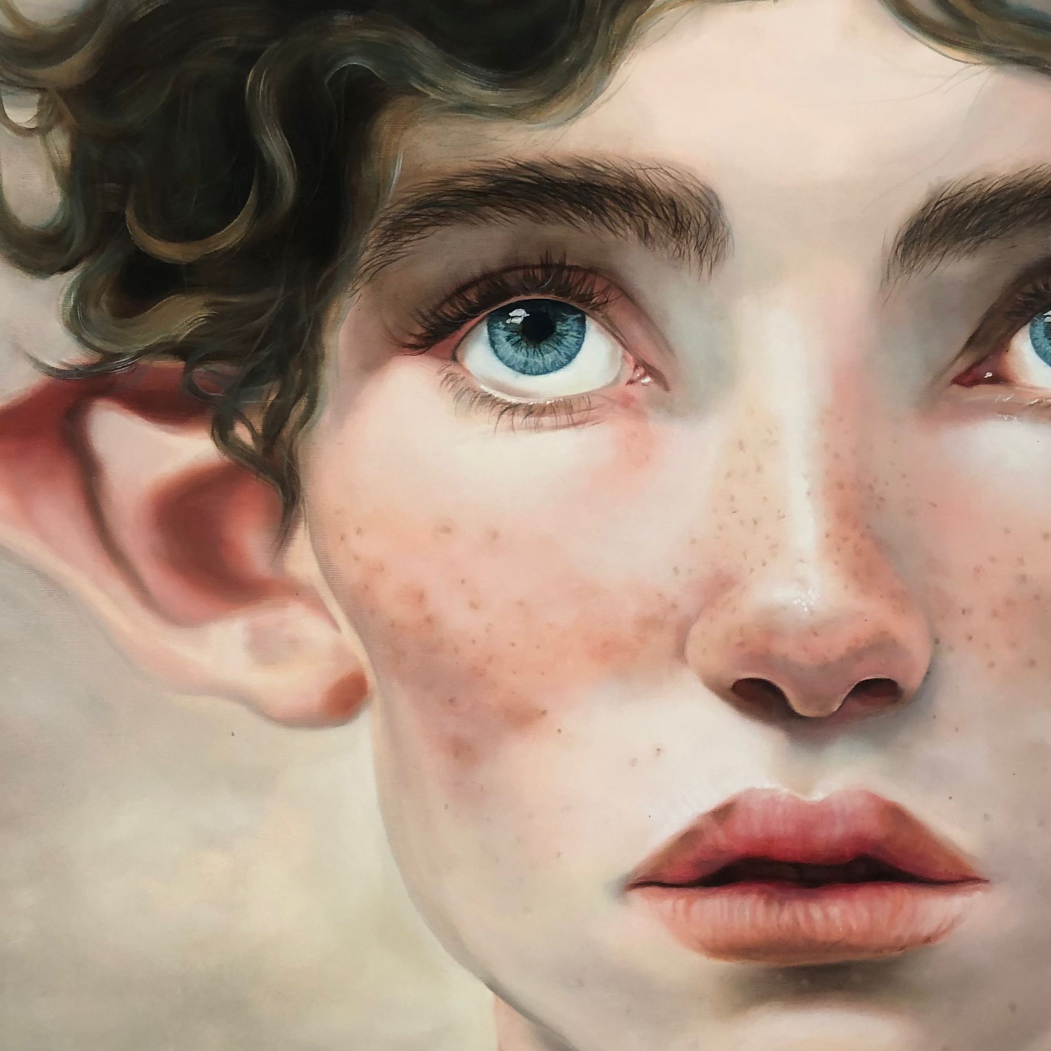 Nahaufnahme eines Gesichts mit blauen Augen, Sommersprossen und lockigem Haar.
