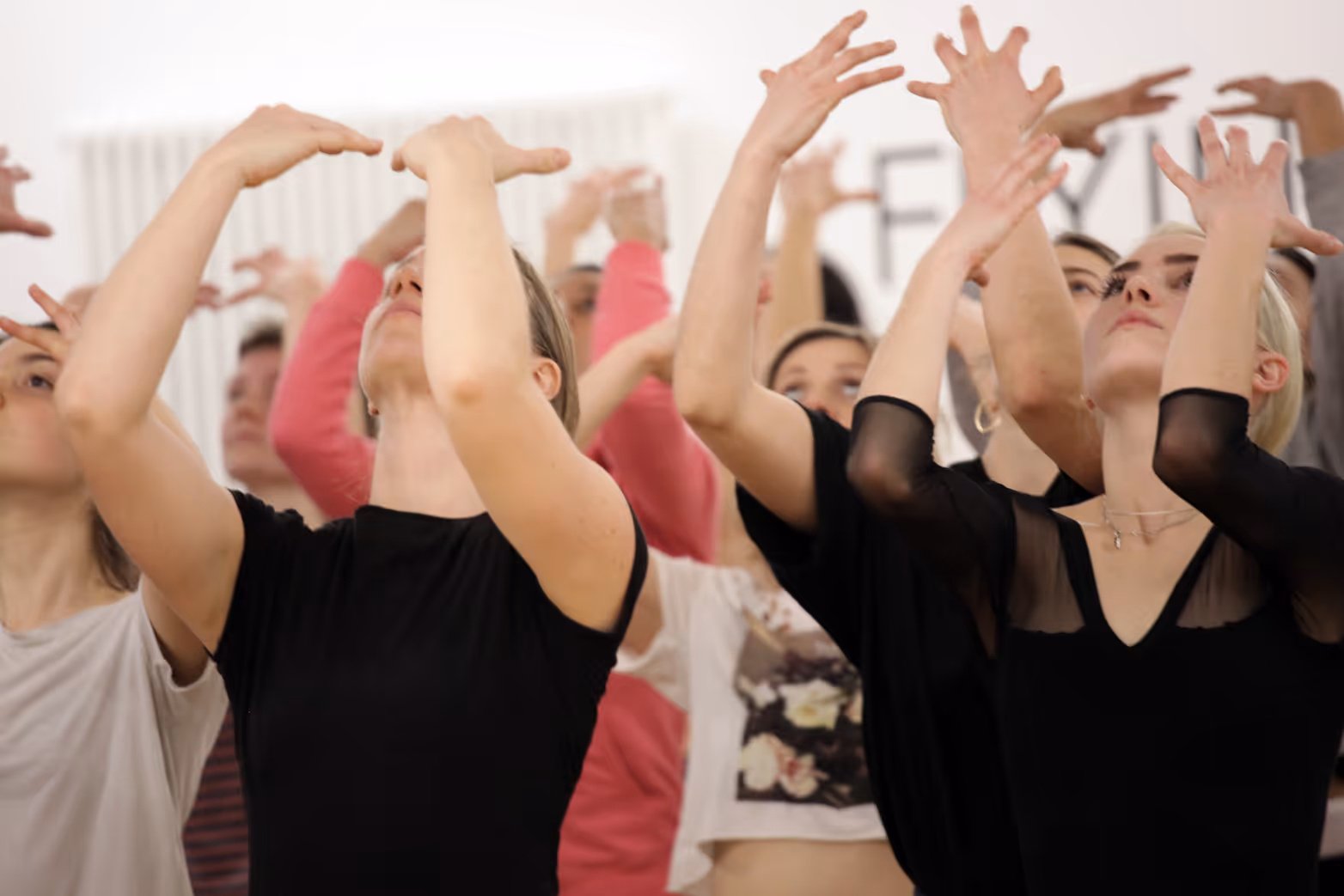 eine Gruppe von Tänzerinnen, die in einem Studio ihre Hände vor das Gesicht halten