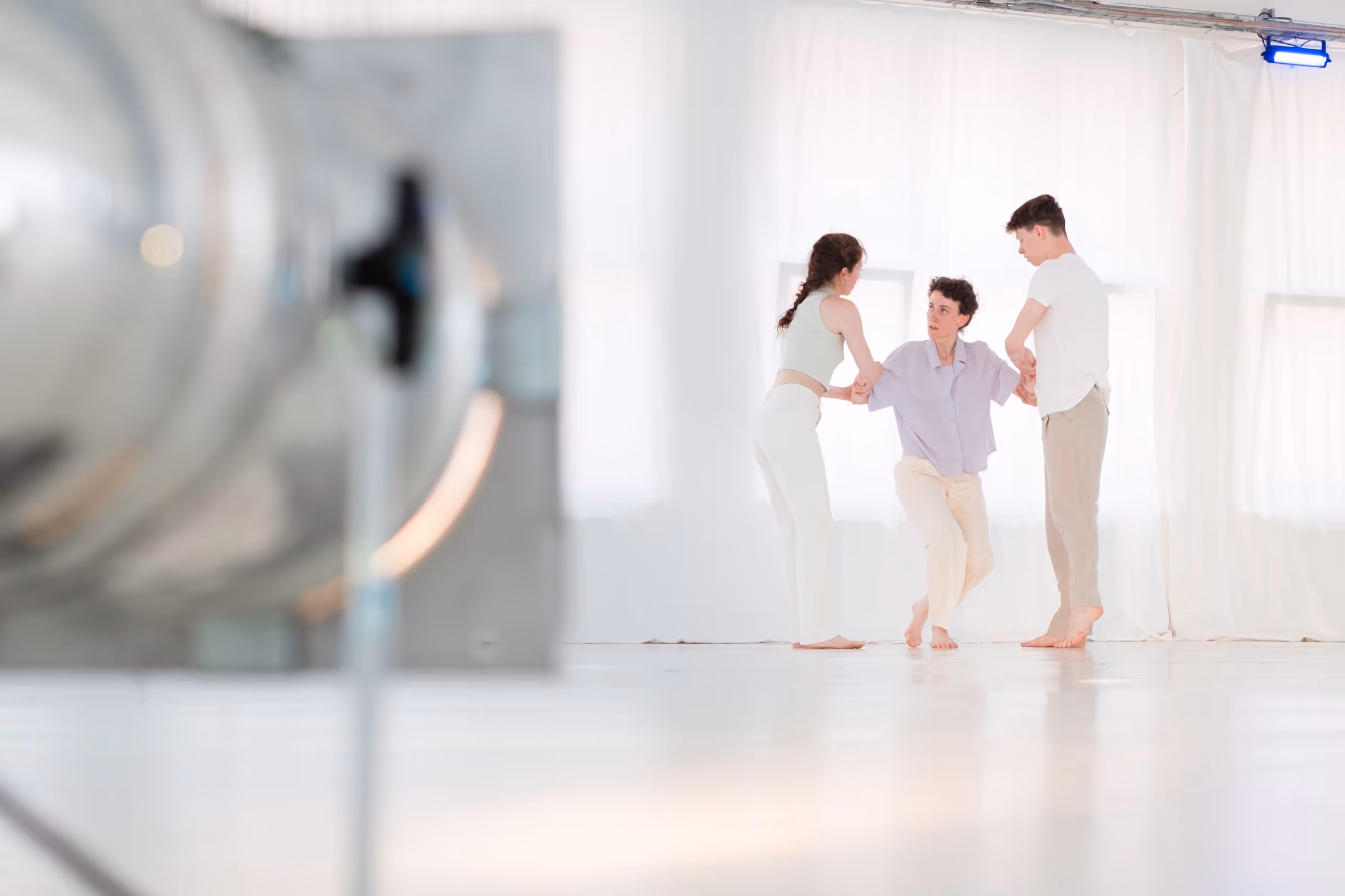 Tänzer:innen, die sich auf einer weißen Studiobühne an den Armen halten
