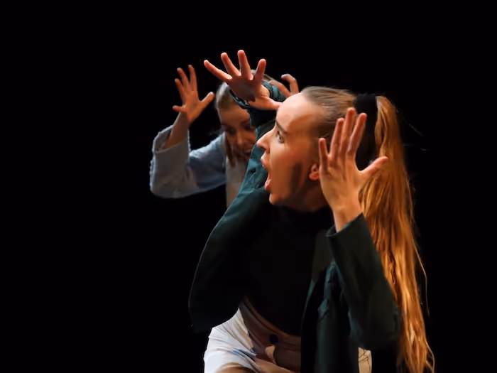 Zwei Darstellerinnen auf der Bühne singen laut, während sie sich die Ohren mit den Händen zuhalten