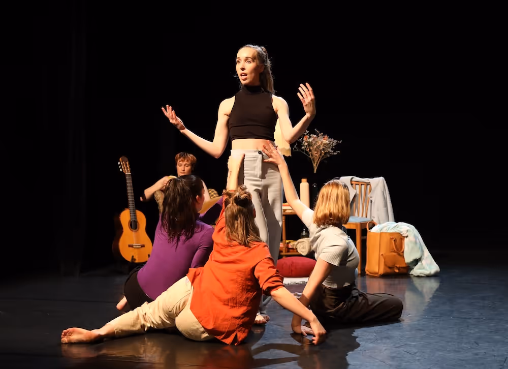 Eine Darstellerin singt auf der Bühne, während drei Darstellerinnen um sie herum sitzen und ihre Hände zu ihr erheben