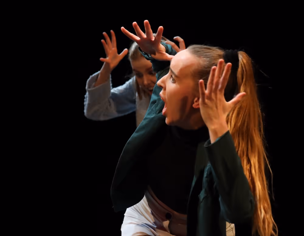 Zwei Darstellerinnen auf der Bühne singen laut, während sie sich die Ohren mit den Händen zuhalten