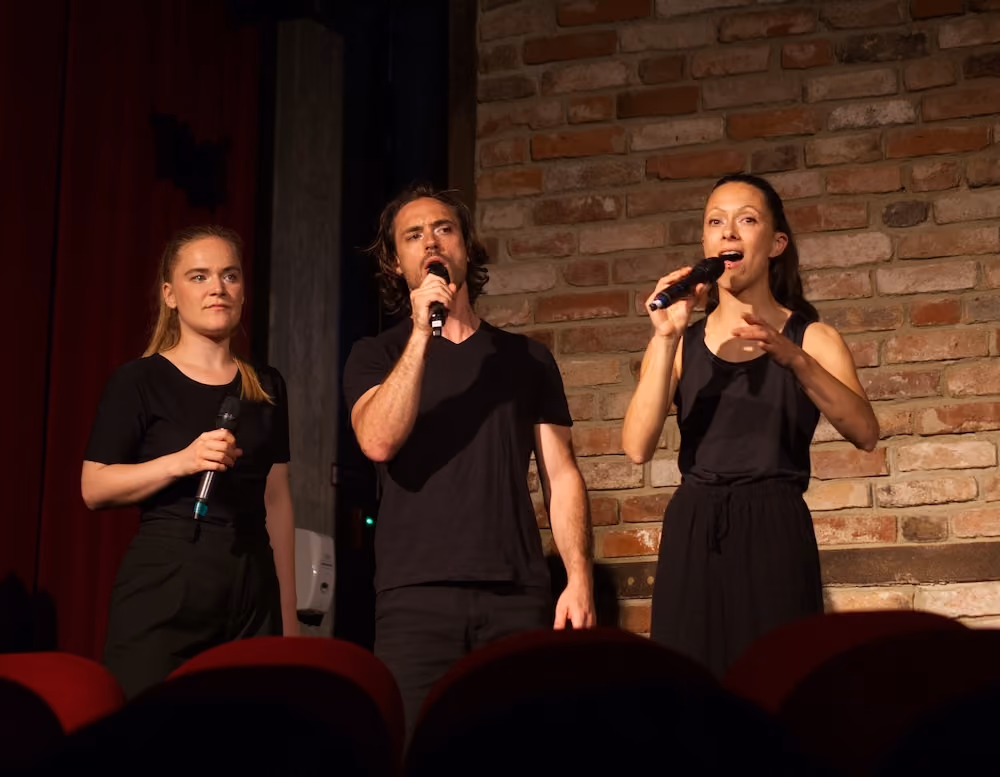 Eine Darstellerin singt auf der Bühne, während drei Darstellerinnen um sie herum sitzen und ihre Hände zu ihr erheben