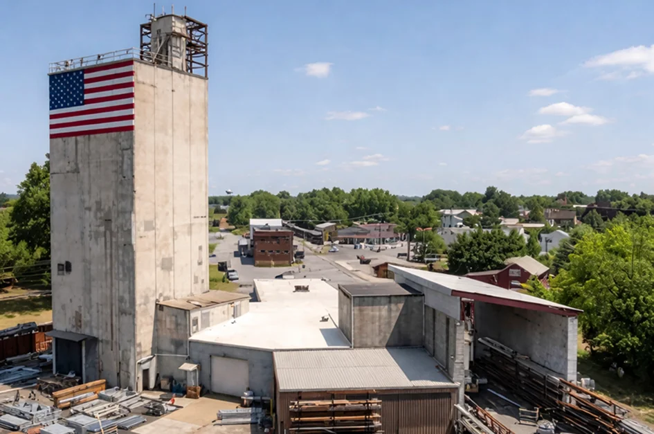 Industrial building with large American flag on tall concrete tower under blue sky.