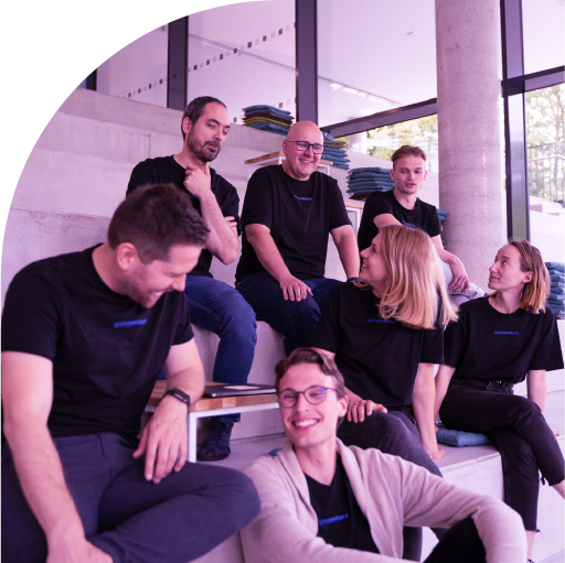Seven casually dressed people sitting and chatting on wide concrete steps inside a building with large windows.