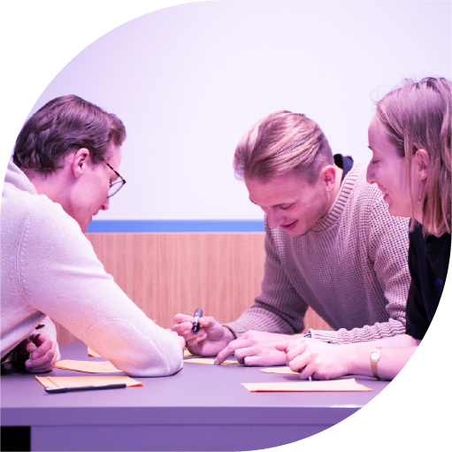 Three people sitting at a table engaged in a discussion and writing on sticky notes.