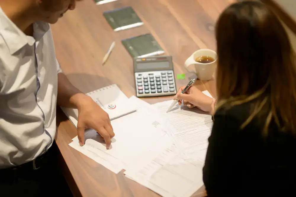 Two colleagues working through documents with a calculator