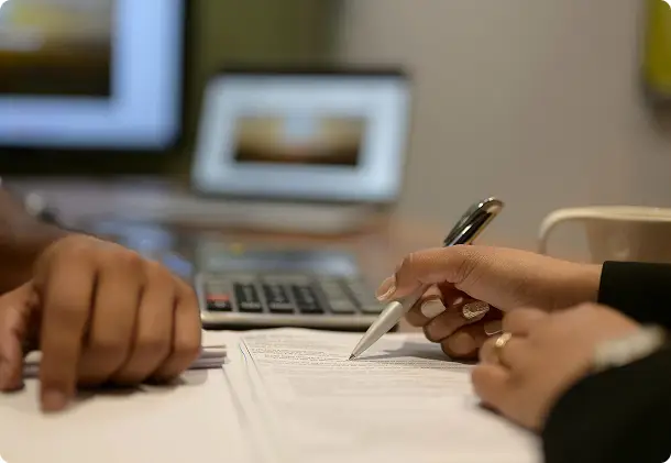 Close-up of hands signing documents beside a laptop