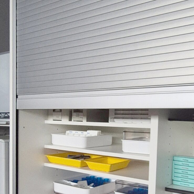 Medikamentenschrank mit geöffnetem Rollladen und beleuchteten, geordneten Tablaren