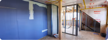 Innenansicht einer Baustelle mit teilweise verputzten Wänden, Holzstützen und einem Türrahmen aus Metall.