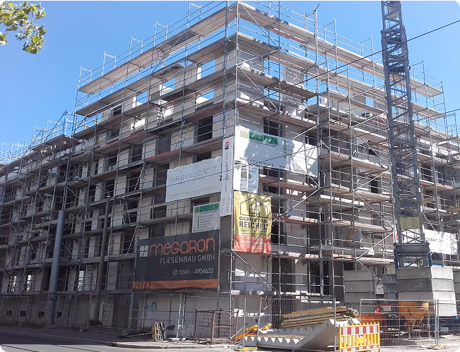 Mehrstöckiges Gebäude in Rohbauphase mit umlaufendem Gerüst bei klarem Himmel.