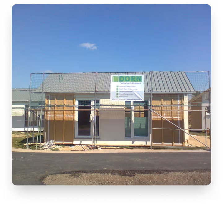 Haus im Rohbau mit Gerüst und Werbebanner der Baufirma DORN vor blauem Himmel.