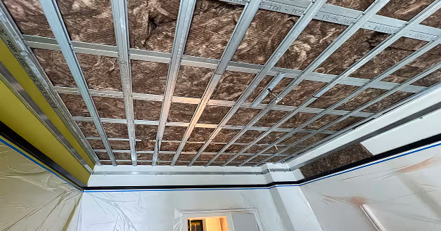 Decke im Rohbau mit Metallprofilen und brauner Dämmung, Wände mit Plastikfolie zum Schutz abgedeckt.