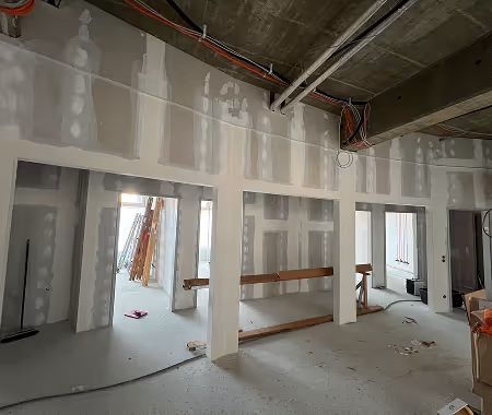 Innenaufnahme einer Baustelle mit weißen, unfertigen Trockenbauwänden und sichtbarer Betondecke.