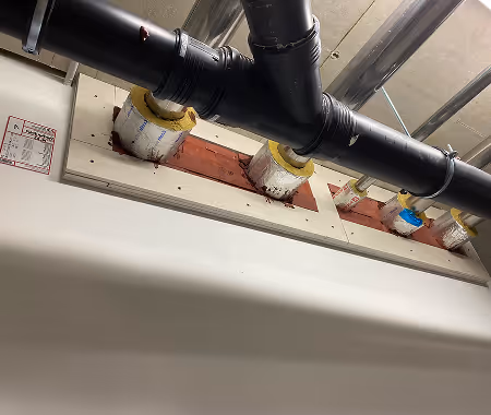 Schwarzes Lüftungsrohr mit Verbindungsstück über isolierten Rohrdurchführungen in einer Betondecke.