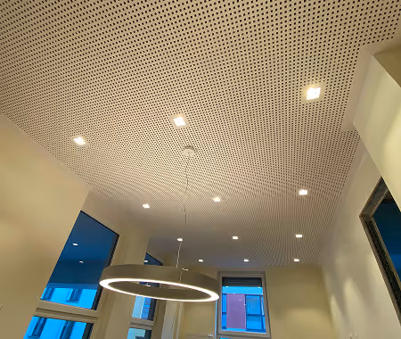 Innenraum mit perforierter Decke, mehreren eingebauten Deckenleuchten und einem runden hängenden LED-Licht über einem Fenster.