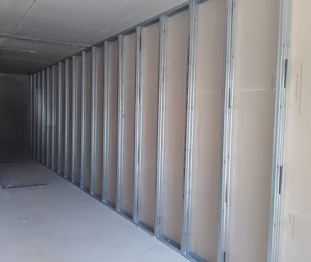 Innenraum im Rohbau mit einer Wandverkleidung aus Metallständern und Gipskartonplatten.