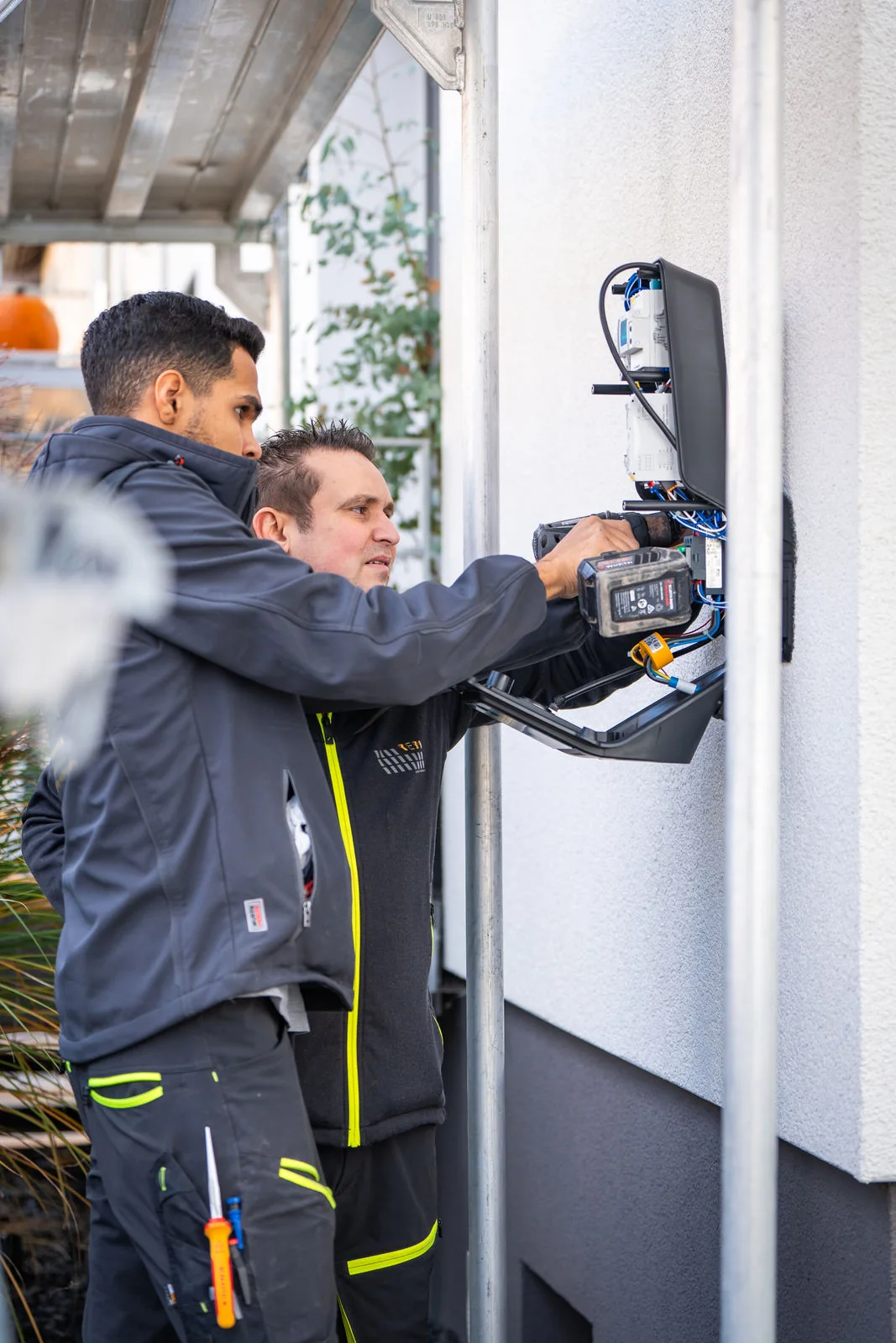 2 Mitarbeiter von Reba Solar installieren eine Wallbox an einer Hauswand 