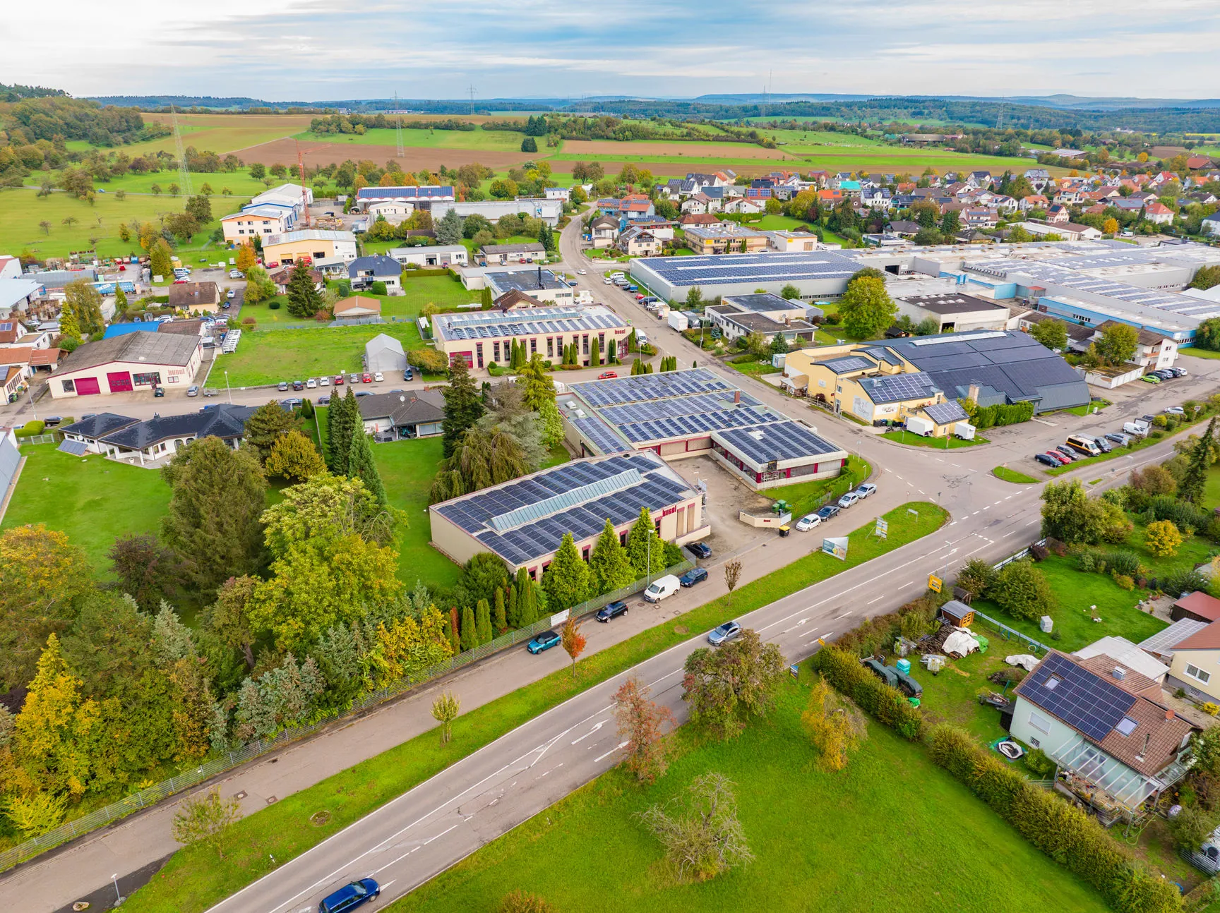 Luftaufnahme eines Gewerbegebiets mit Fokus auf mehrere große Industriehallen, deren Flachdächer großflächig mit Photovoltaikanlagen ausgestattet sind.