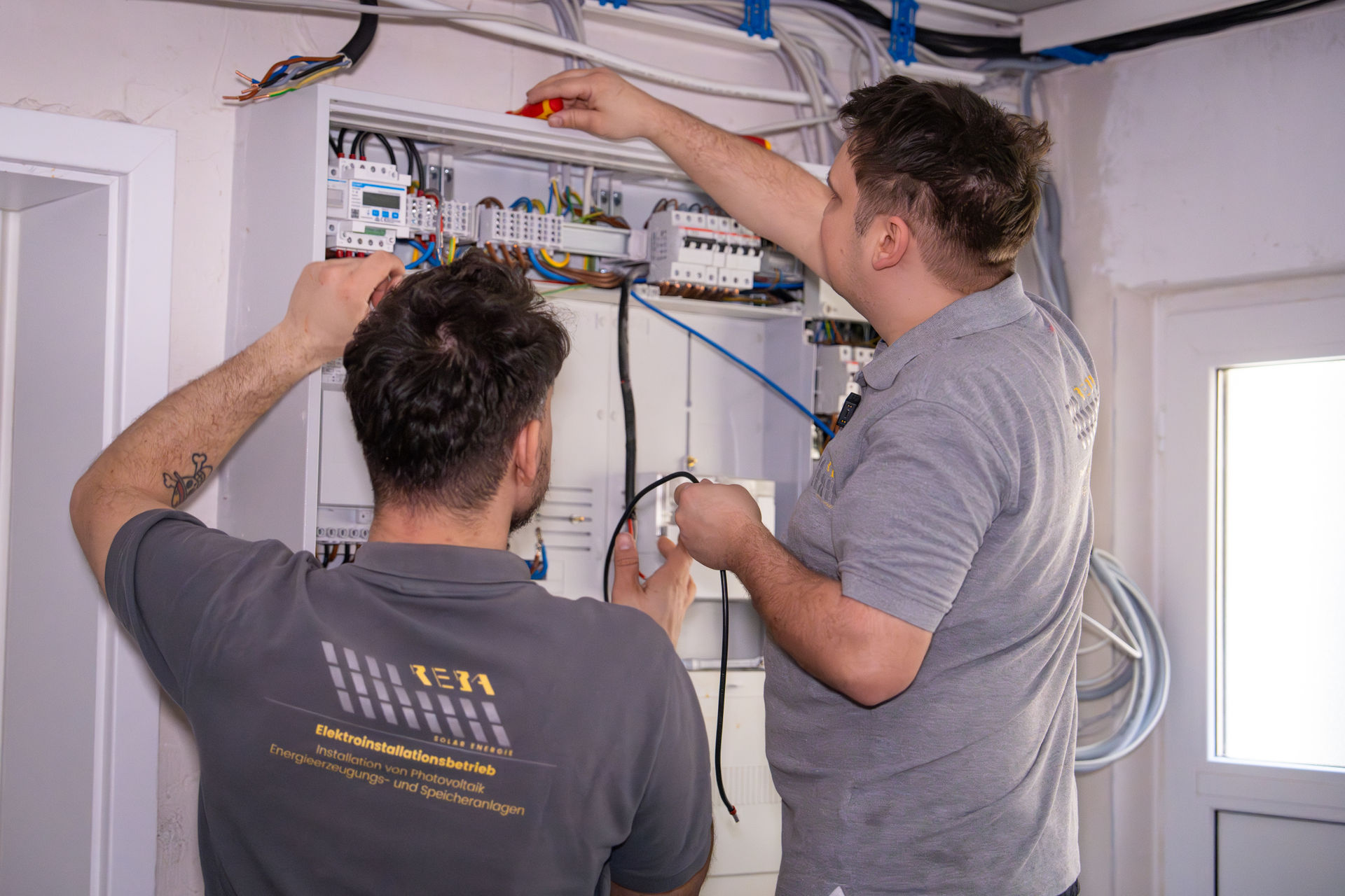 Zwei Elektroniker von Reba Solar bei der Verdrahtung und Installation eines modernen Schaltschranks für eine Photovoltaikanlage.