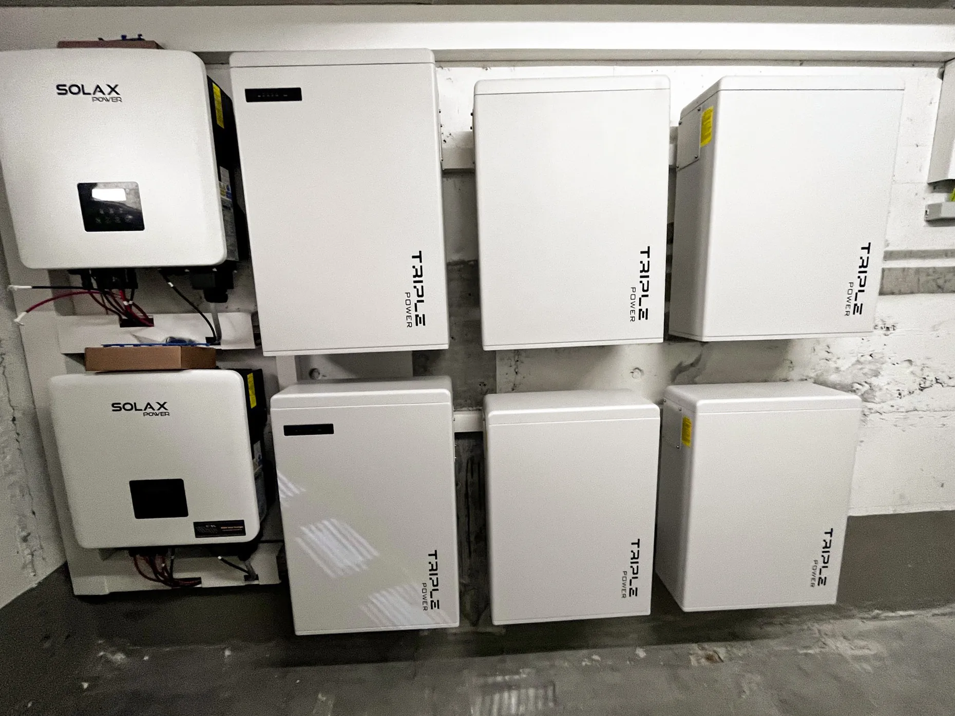 Professionelle Installation von SolaX Power Wechselrichtern und Triple Power Batteriespeichern an einer Kellerwand. Die weißen Photovoltaik-Komponenten sind sauber in zwei Reihen montiert.