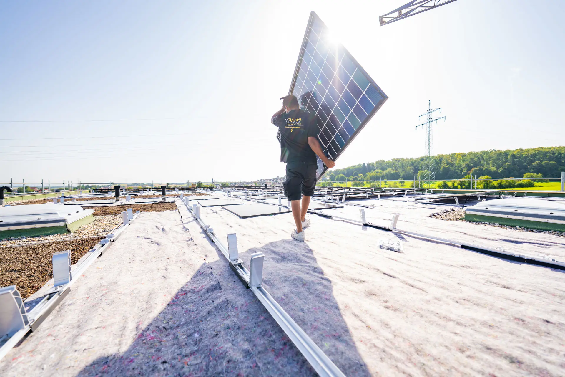 Ein Monteur trägt ein Solarmodul während der Installation einer Photovoltaik-Anlage auf einem großen Dach.