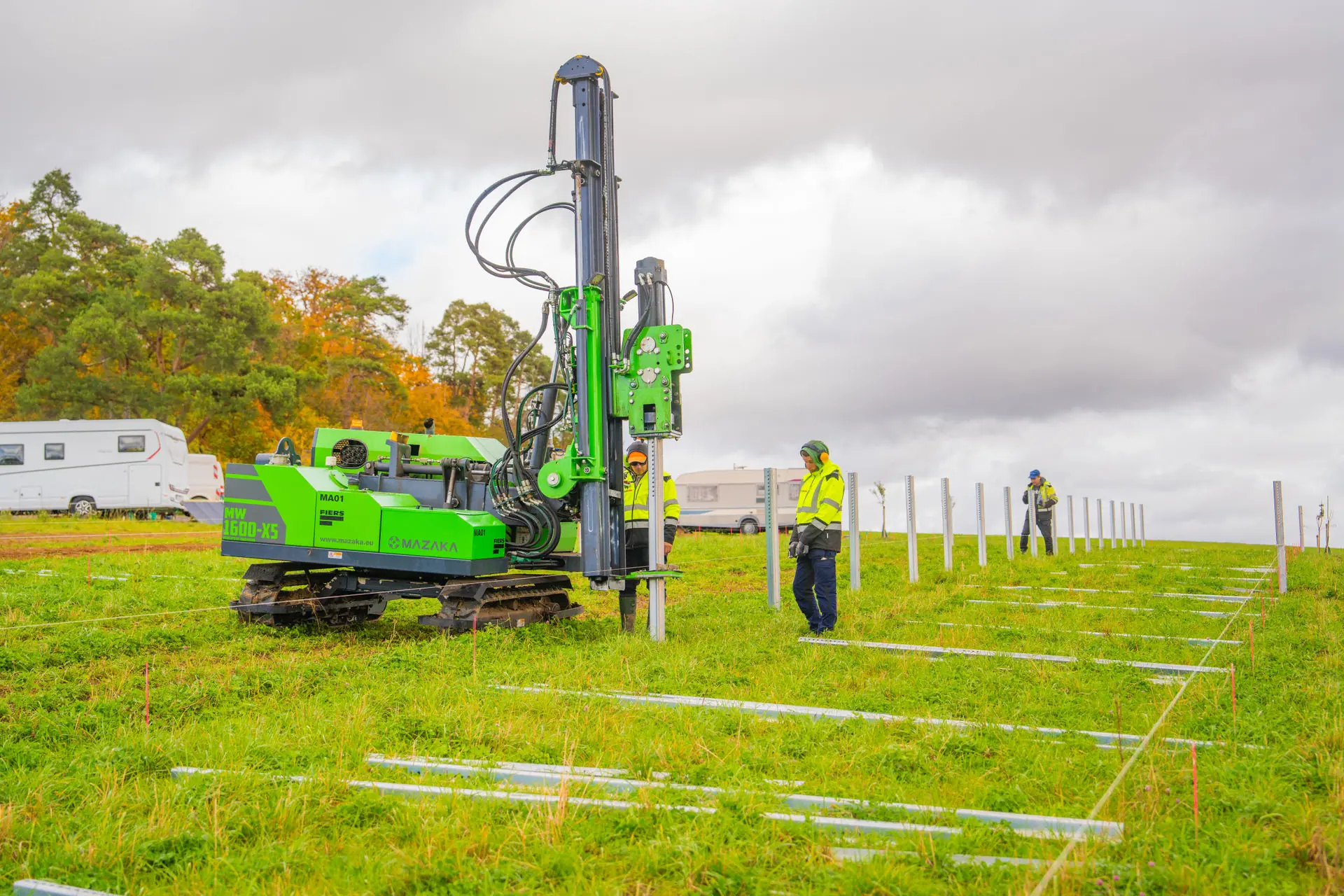 Präziser Bau eines Solarparks: Spezialmaschine rammt Stützpfeiler für die Modulunterkonstruktion auf einer großen Freifläche. Experten der Firma koordinieren den Einbau der Komponenten.