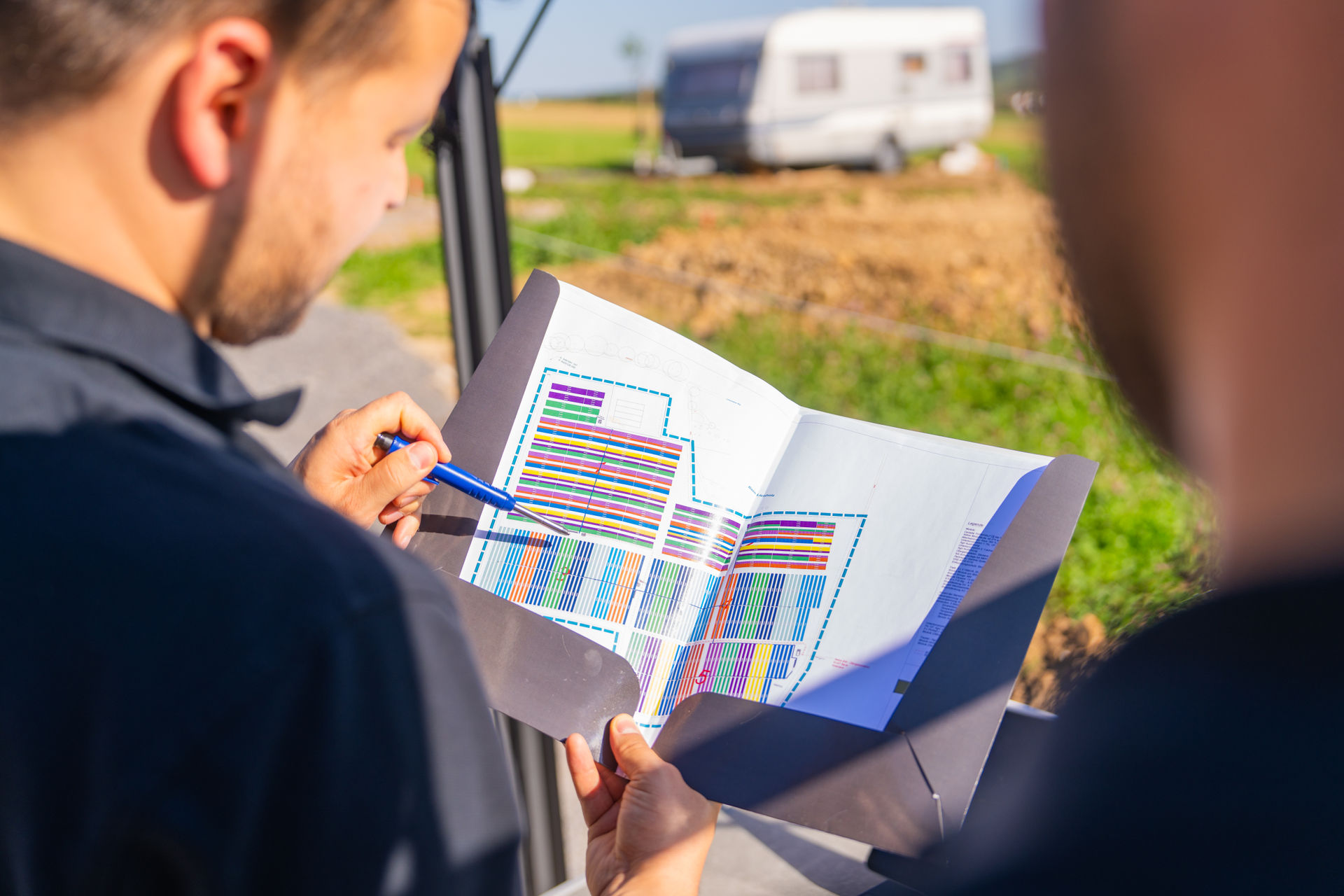 Detailaufnahme einer Vor-Ort-Besprechung: Das Reba Team analysiert die detaillierte Flächenplanung einer Photovoltaik-Anlage. Der Plan zeigt die Anordnung der Modulreihen in verschiedenen Farben.