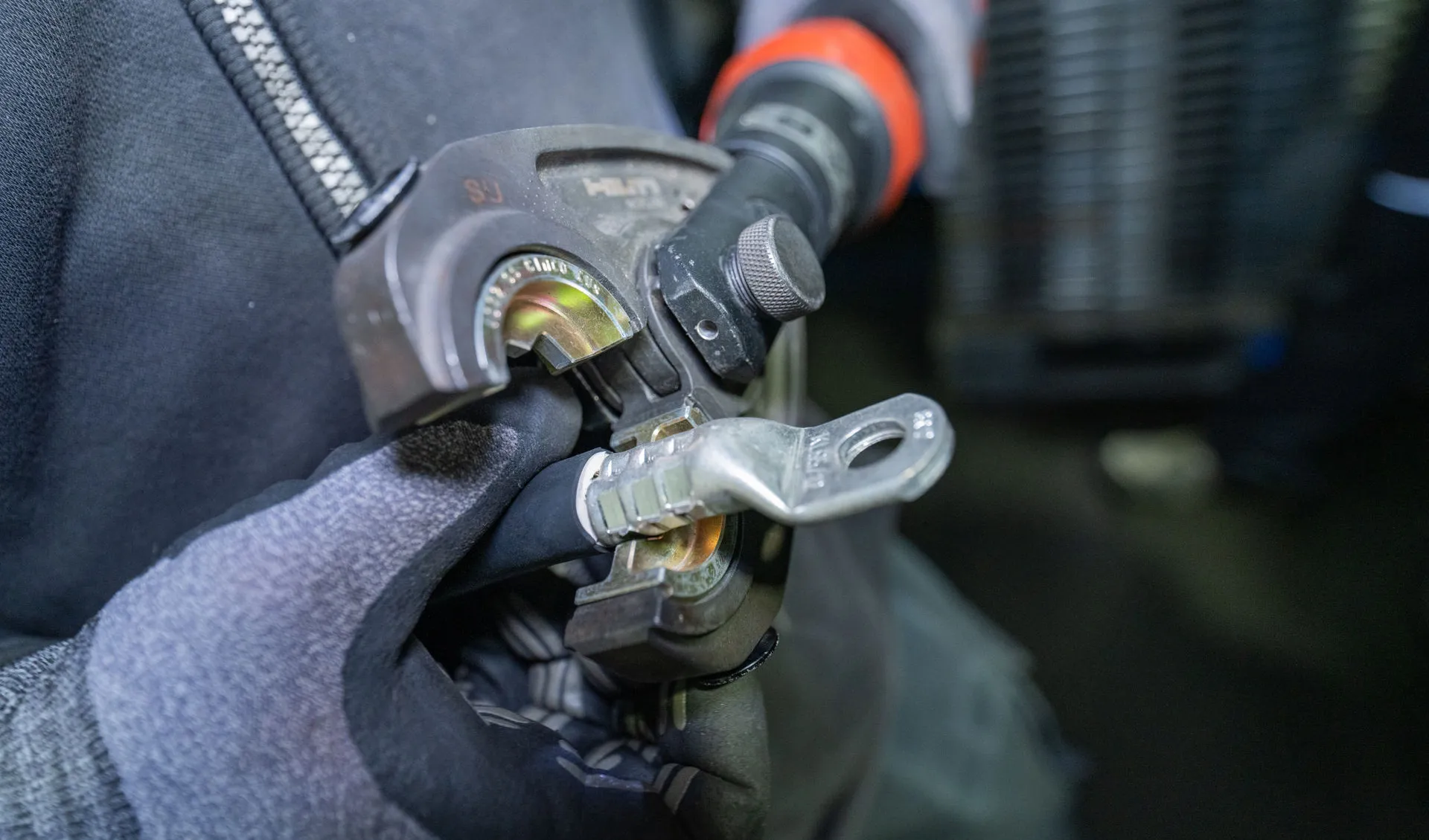 Fachgerechtes Verpressen eines Kabelschuhs mit einem hydraulischen Crimpwerkzeug an einem Starkstromkabel in Nahaufnahme.