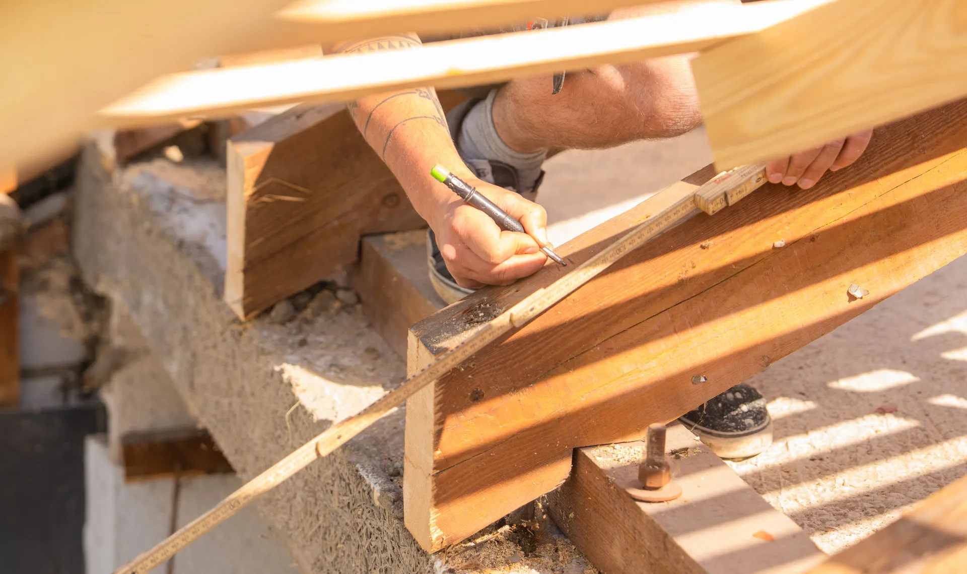 Nahaufnahme eines Zimmerers, der mit einem Bleistift und einem Holz-Zollstock Markierungen auf einem massiven Dachbalken für die Sanierung anzeichnet.