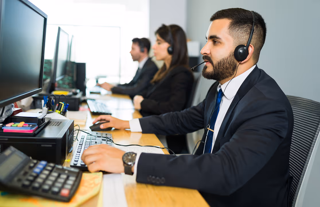 Three customer service representatives wearing headsets working on computers in an office.