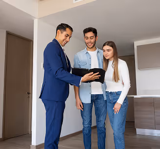 Man in suit showing a tablet to a casually dressed young couple inside a home.