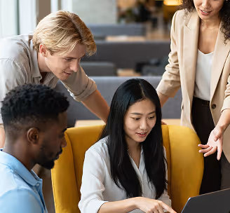 Four diverse coworkers collaborating and looking at a laptop in a modern office setting.