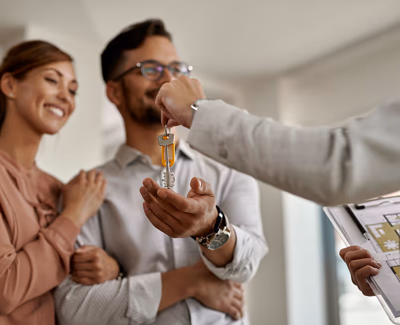 Real estate agent handing over house keys to smiling couple inside a new home.