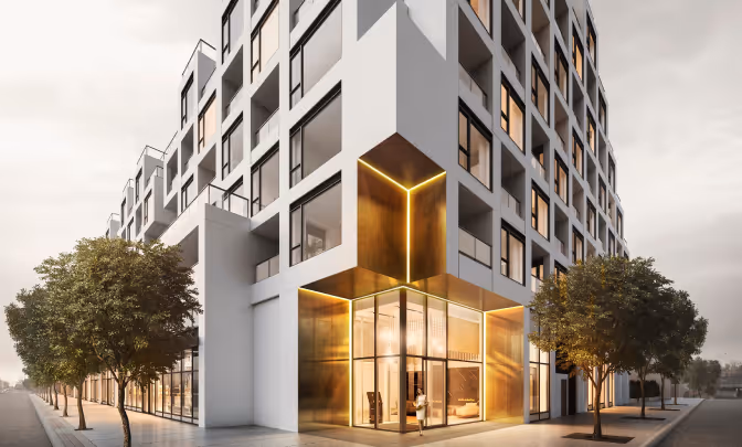 Modern multi-story building with illuminated golden entrance and trees on the sidewalk at dusk.