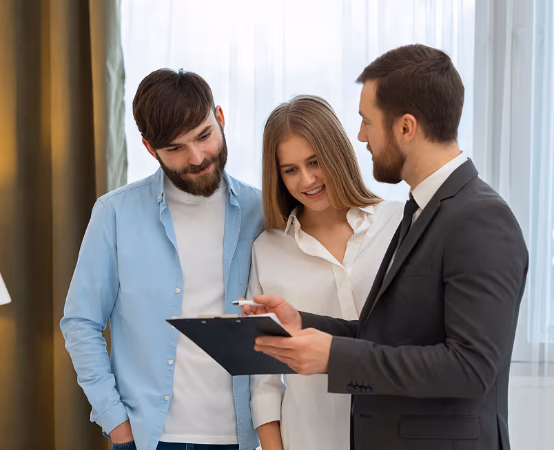 Man in suit showing clipboard to smiling couple in casual clothes in a bright room.