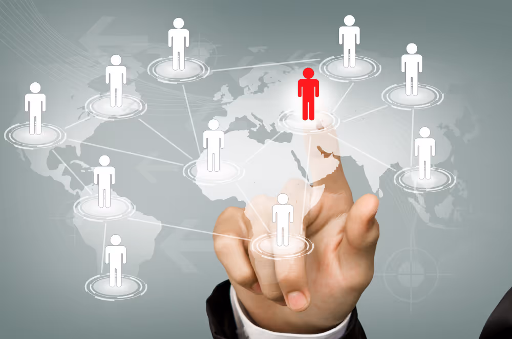 Hand pointing at a red figure among white figures connected by lines on a world map network.